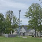 Solar-powered outdoor warning siren on a tall metal pole in a grassy Rossville neighborhood, with trees and homes under an overcast sky.